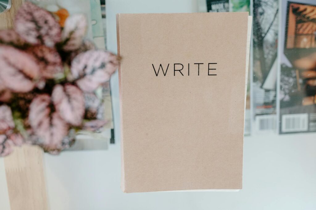 Top view of a notebook labeled 'WRITE' on a glass table with magazines and a potted plant.