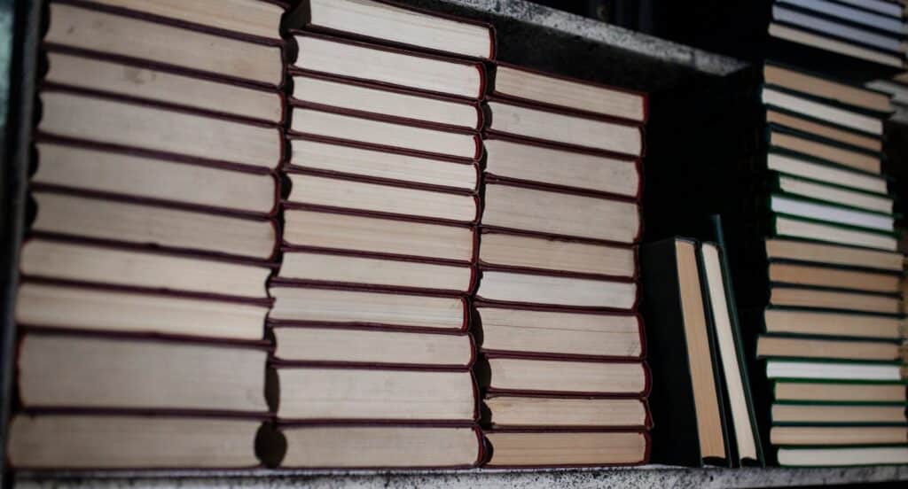 A neat stack of hardcover books on a bookshelf, showing organized bindings.